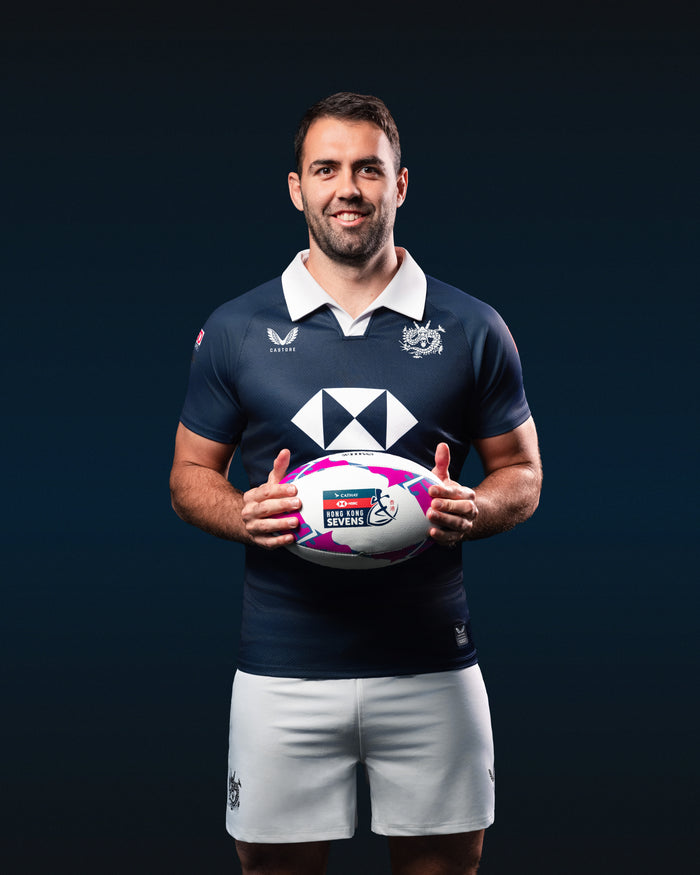 Athlete in navy HK7s home replica jersey holding a rugby ball against a dark backdrop