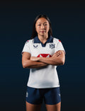 Junior white away jersey with navy collar and chest crest worn by a model.